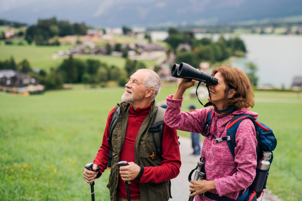 A senior pensioner couple hiking in nature, using binoculars.