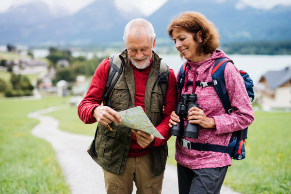 A senior pensioner couple with hiking in nature, using binoculars and map.