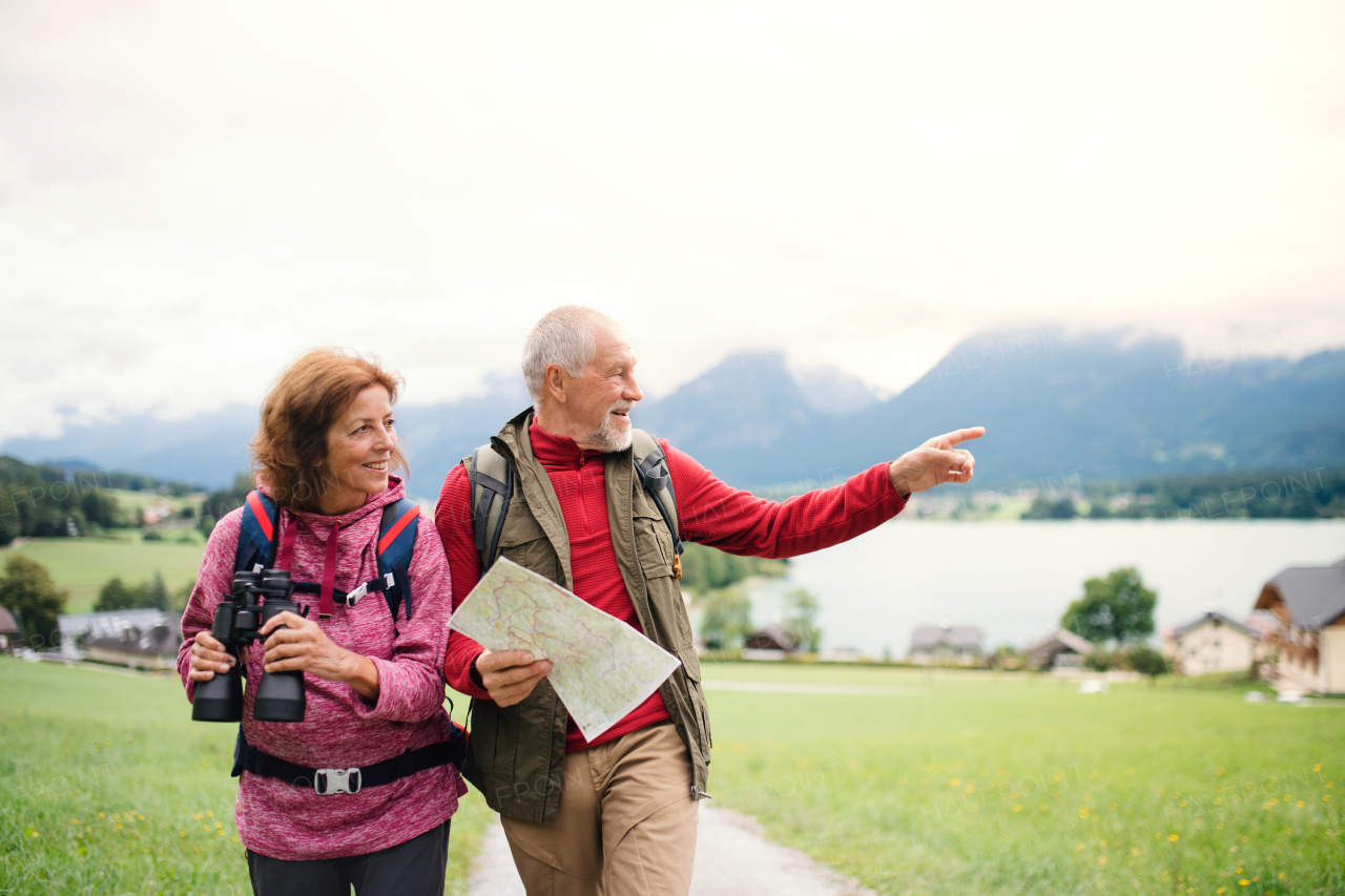 A senior pensioner couple with hiking in nature, using binoculars and map.