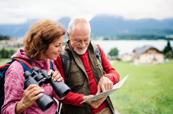 A senior pensioner couple with hiking in nature, using binoculars and map.