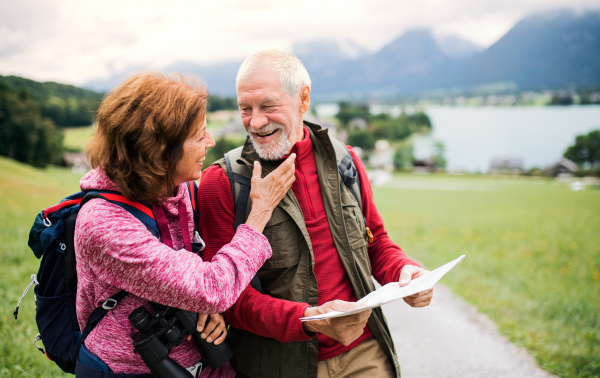 A senior pensioner couple with hiking in nature, using binoculars and map.