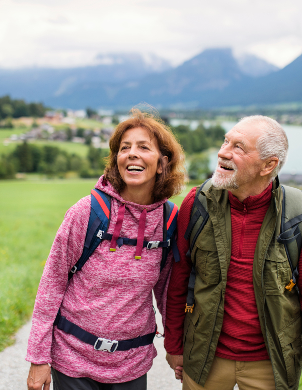 Front view of happy senior pensioner couple hiking in nature, talking.