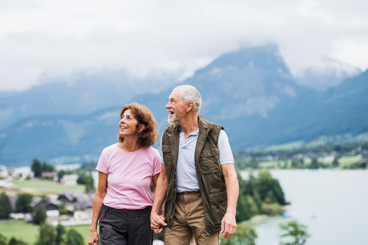 An active senior pensioner couple hiking in nature, holding hands.