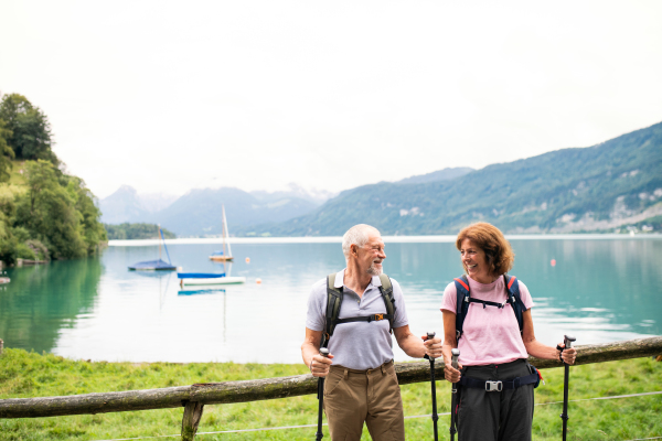 A happy senior pensioner couple with nordic walking poles hiking in nature, resting.