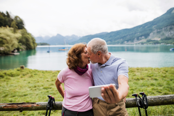 A senior pensioner couple hikers standing in nature, taking selfie when kissing.