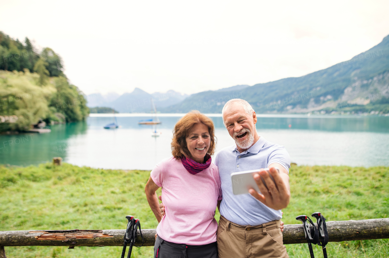 A senior pensioner couple hikers standing in nature, taking selfie.