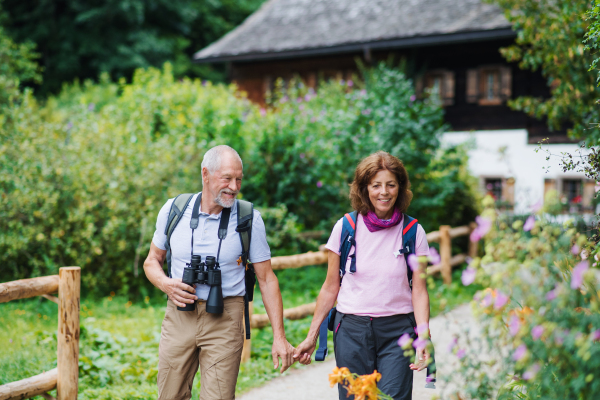 A happy senior pensioner couple with binoculars hiking, holding hands.