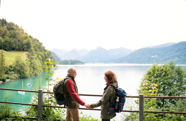 A senior pensioner couple hikers standing by lake in nature, talking. Copy space.