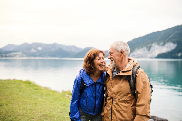 A senior pensioner couple walking by lake in nature, talking. Copy space.