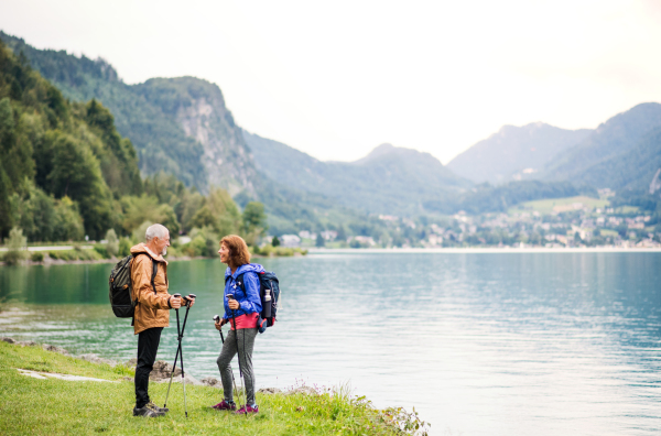 A senior pensioner couple hikers standing by lake in nature, talking. Copy space.