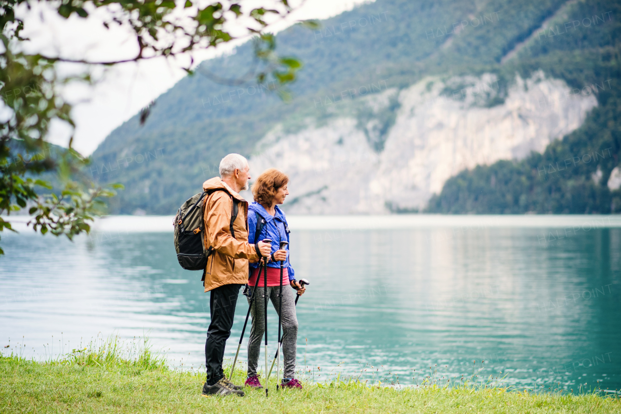 A senior pensioner couple hikers standing by lake in nature, talking. Copy space.