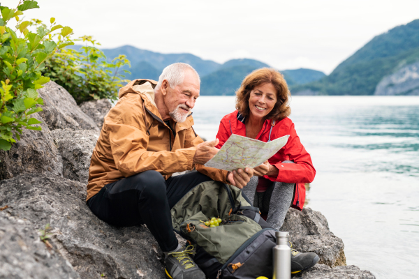 A cheerful senior pensioner couple hiking by lake in nature, using map.