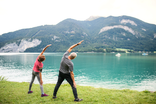 Rear view of senior pensioner couple by lake in nature, doing exercise. Copy space.