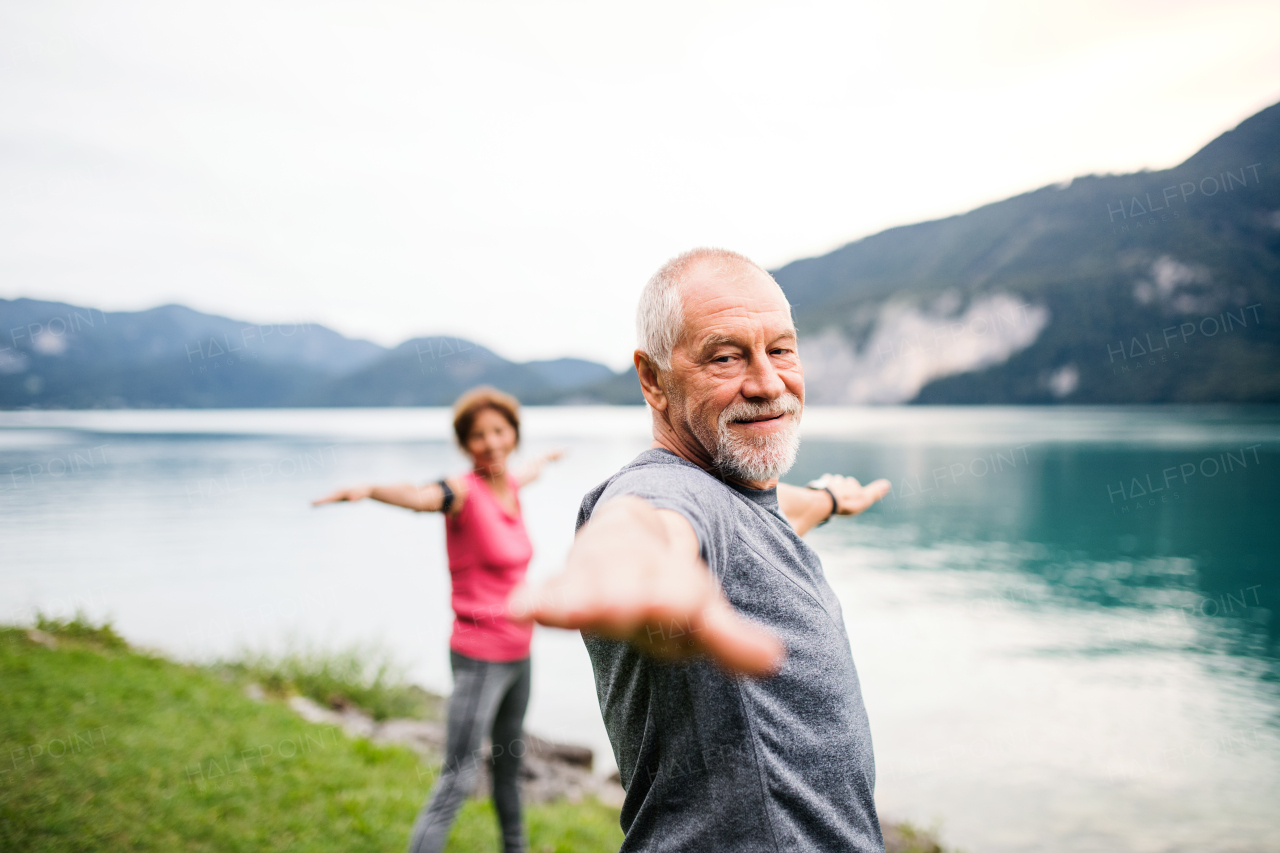 A senior pensioner couple doing exercise by lake in nature, stretching.