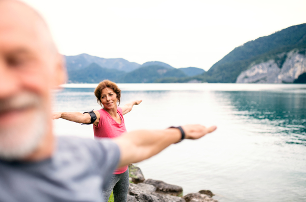 A senior pensioner couple doing exercise by lake in nature, stretching.