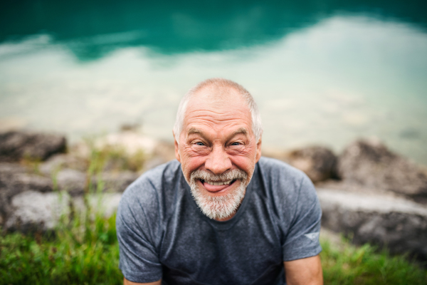 A front view portrait of senior man pensioner standing outdoors in nature, grimacing.