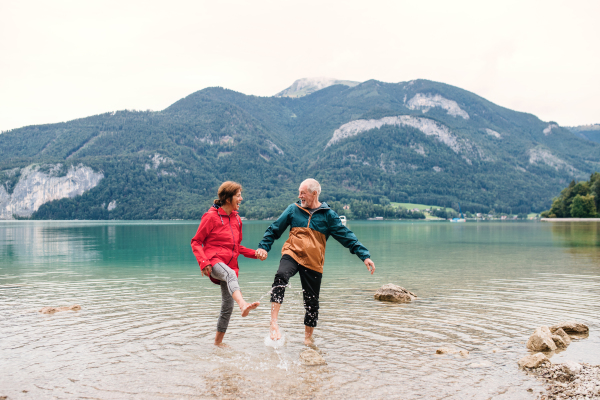 A senior pensioner couple hikers standing barefoot in mountain lake in nature.