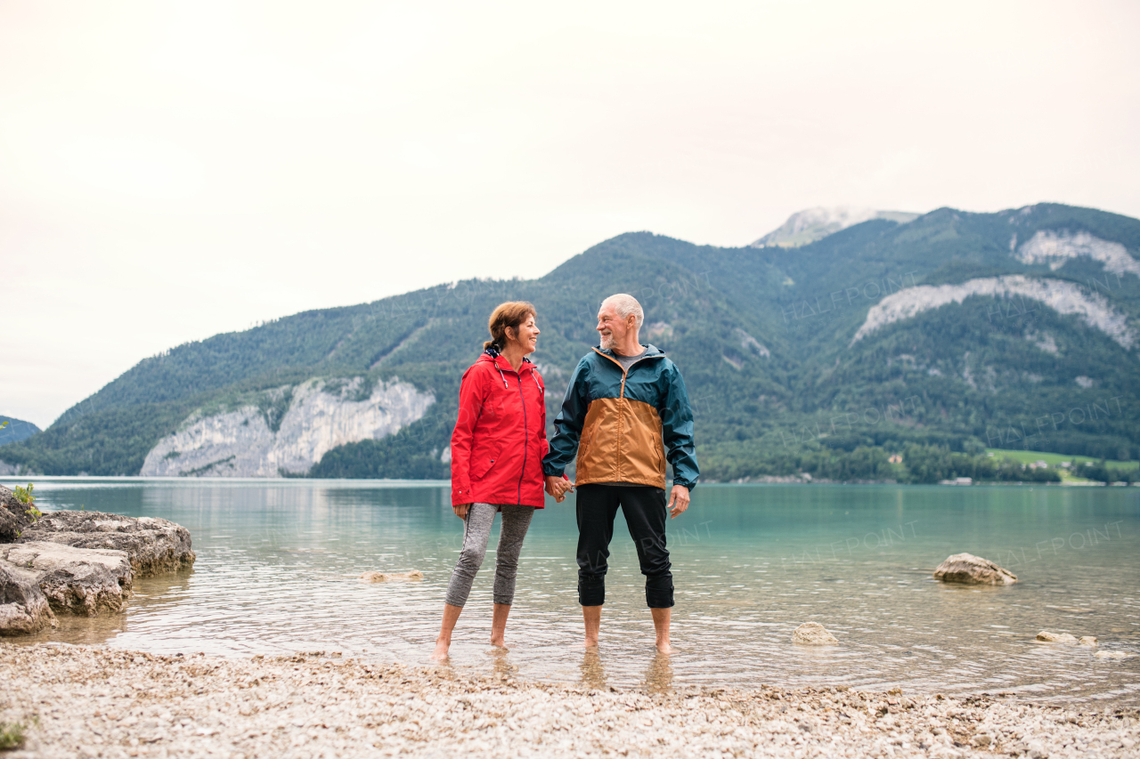 A senior pensioner couple hikers standing barefoot in mountain lake in nature.