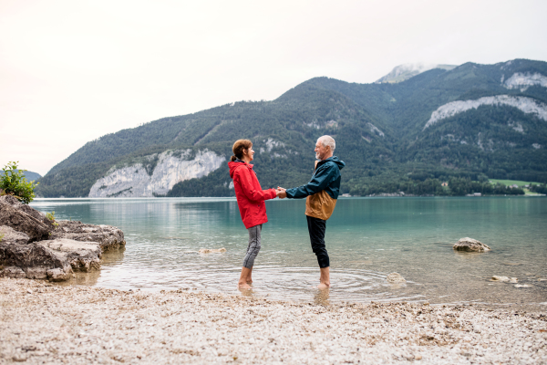 A senior pensioner couple hikers standing barefoot in mountain lake in nature.