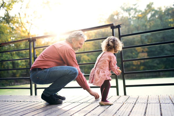 Mature father with toddler daughter standing by the lake on a walk in autumn nature.