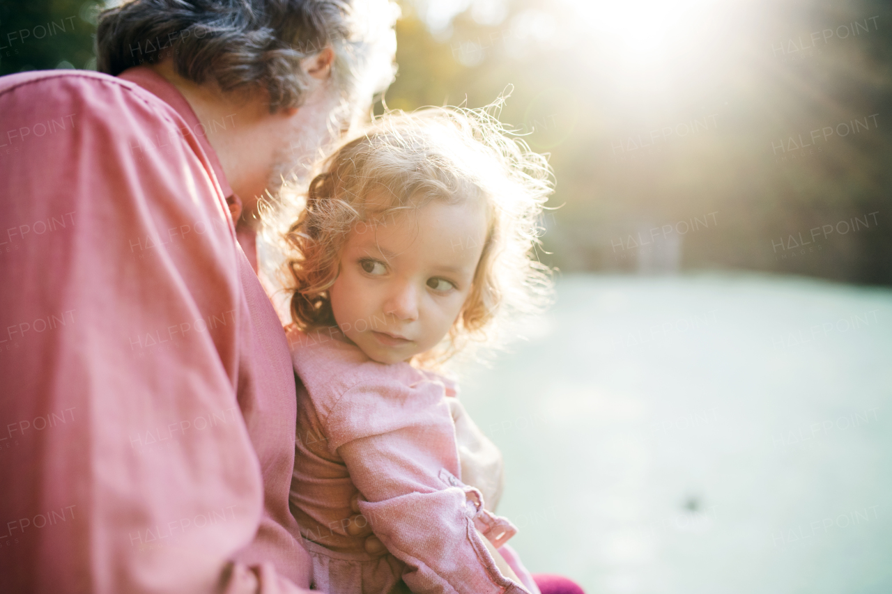 Mature fatherwith toddler daughter standing by the lake on a walk in autumn nature.