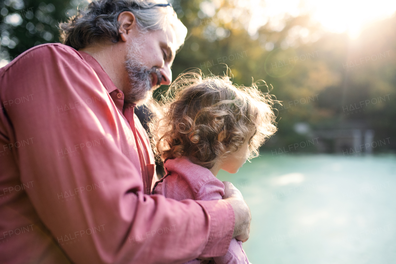 Mature father with toddler daughter standing by the lake on a walk in autumn nature.