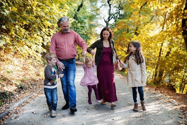 A beautiful young family with small children on a walk in autumn forest, holding hands.