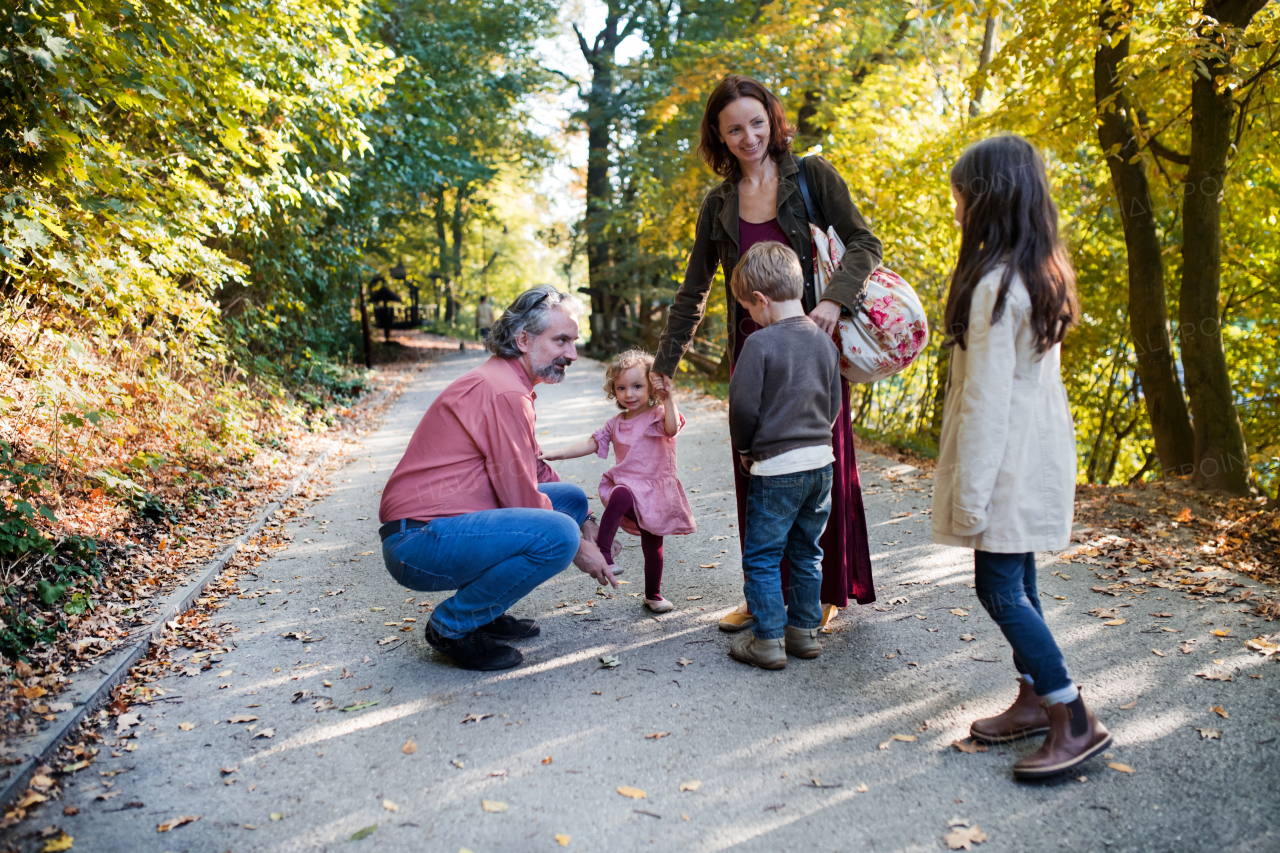 A beautiful young family with small children on a walk in autumn forest, talking.