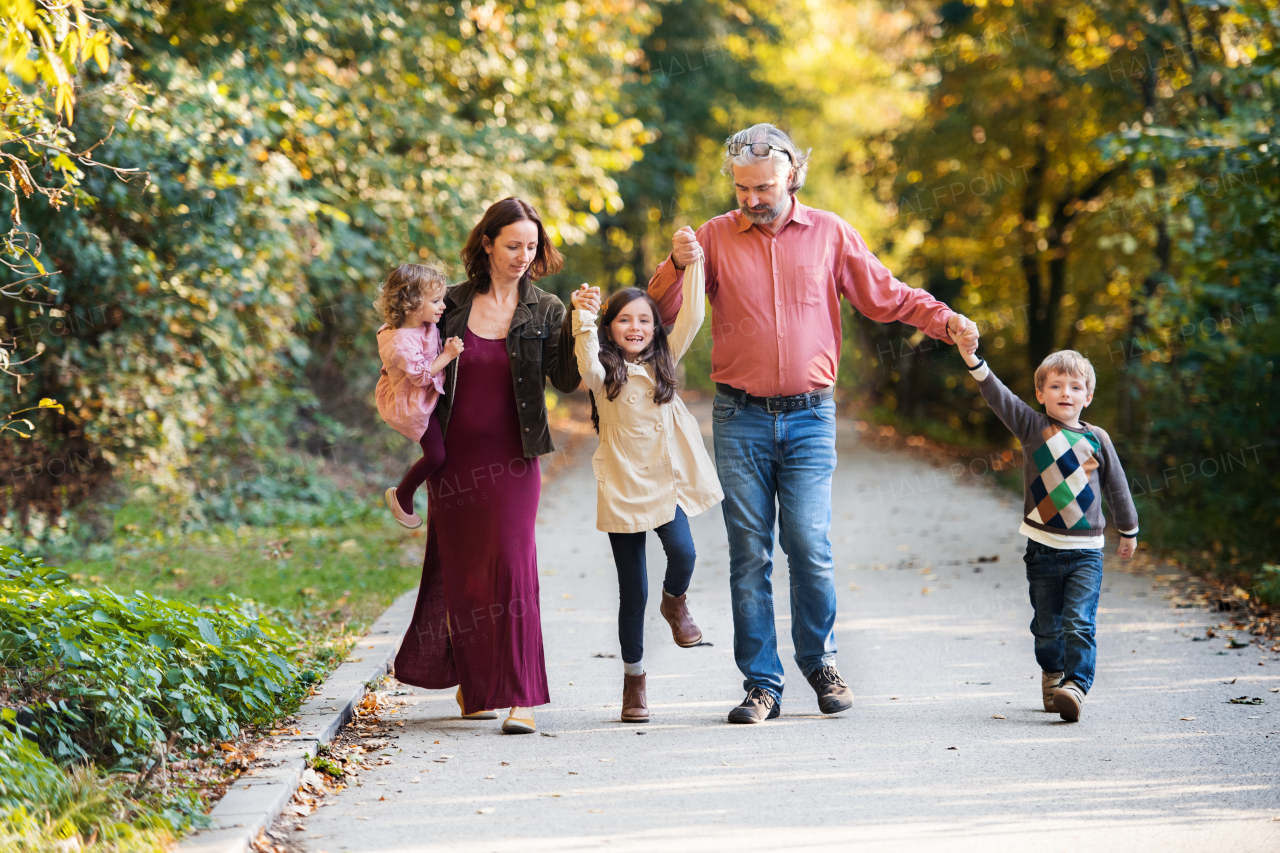 A beautiful young family with small children on a walk in autumn forest, holding hands.