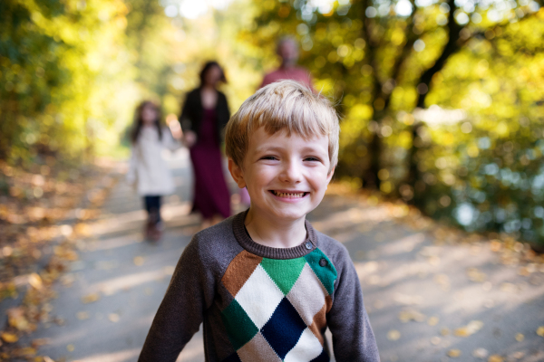 A small boy with his family on a walk in autumn forest, looking at camera.