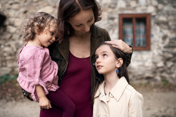 A happy mother with two small daughters standing in front of old stone house.