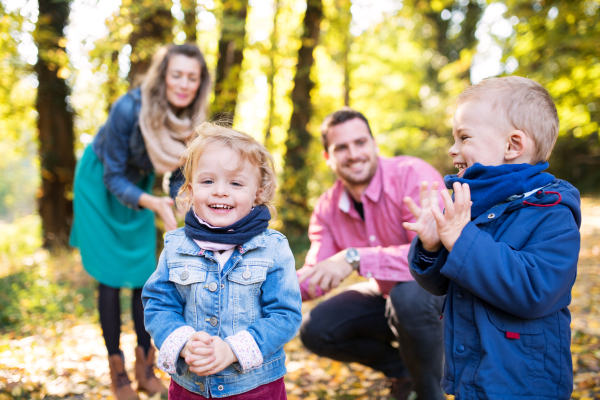 A beautiful young family with small twins on a walk in autumn forest, playing.