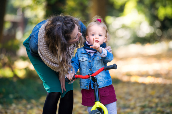 Mother and small daughter with a balance bike on a walk in autumn forest, talking.