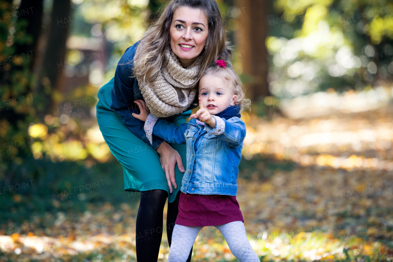 Mother and small daughter on a walk in autumn forest, talking.