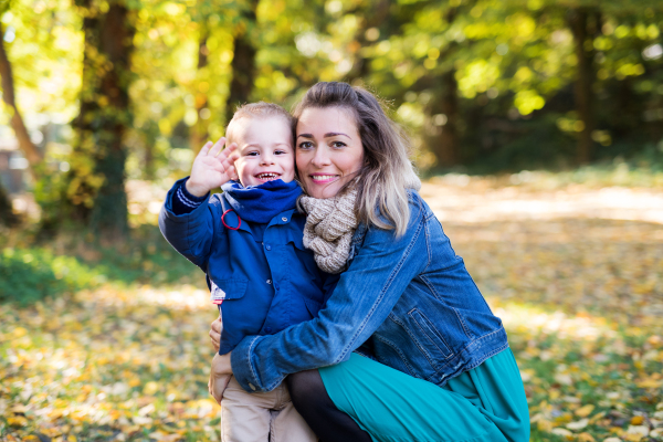 Beautiful young mother with small toddler son on a walk in autumn forest, resting.