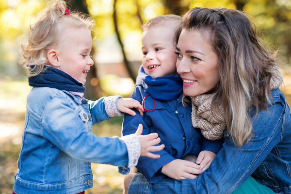 A beautiful young mother with small twins on a walk in autumn forest.