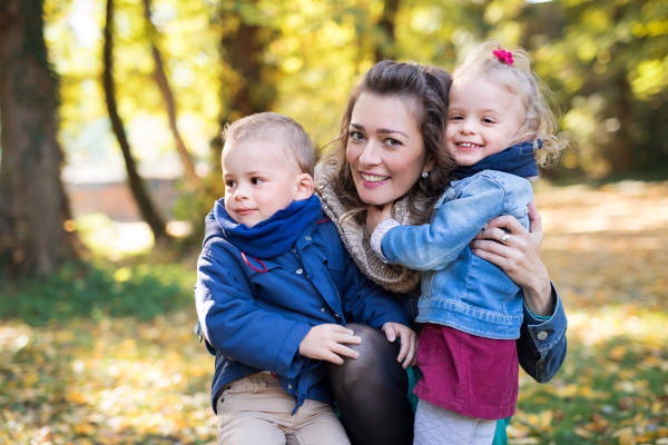 A beautiful young mother with small twins on a walk in autumn forest.