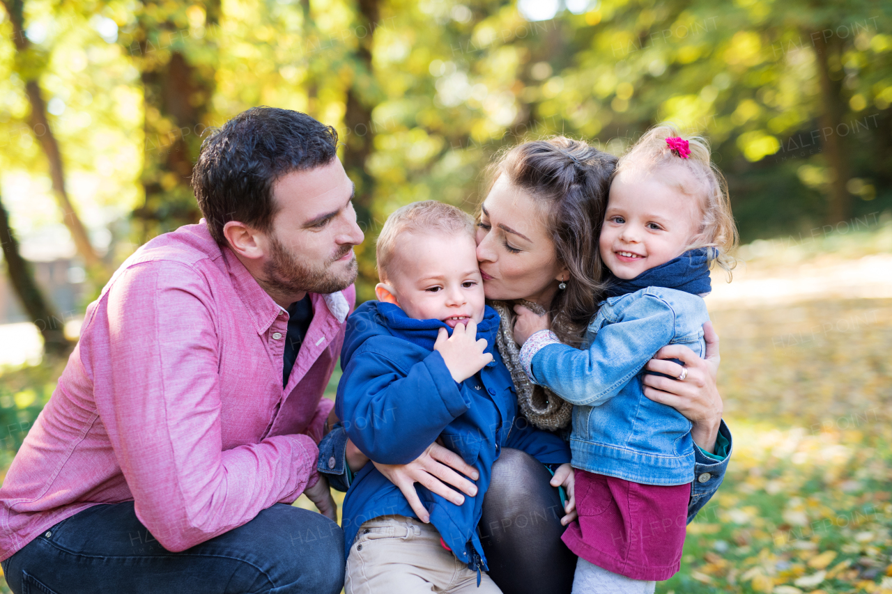 A beautiful young family with small twins on a walk in autumn forest, kissing.