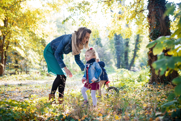 A beautiful young mother with small twins on a walk in autumn forest.