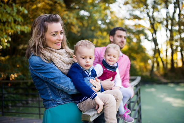 A beautiful young family with small twins on a walk in autumn park, standing by lake.