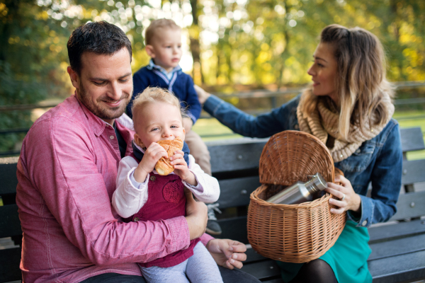 A beautiful young family with small twins on a walk in autumn park, sitting on bench.