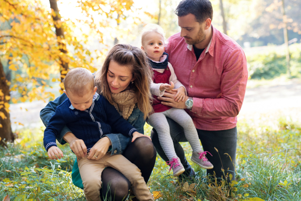 A portrait of beautiful young family with small twins on a walk in autumn forest, resting.