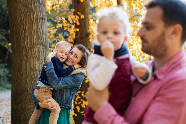 A beautiful young family with small twins on a walk in autumn forest, standing.