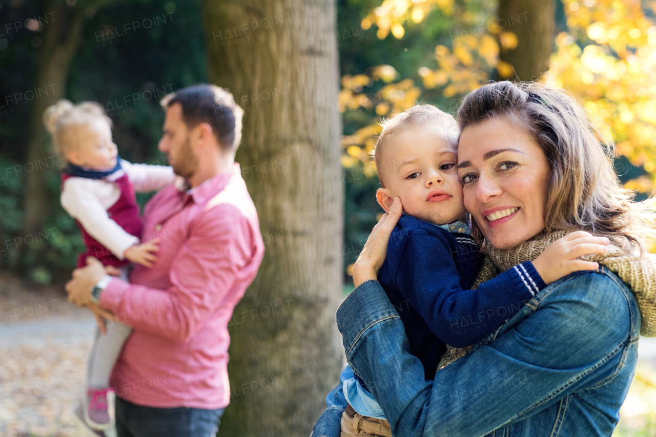 A beautiful young family with small twins on a walk in autumn forest, standing.