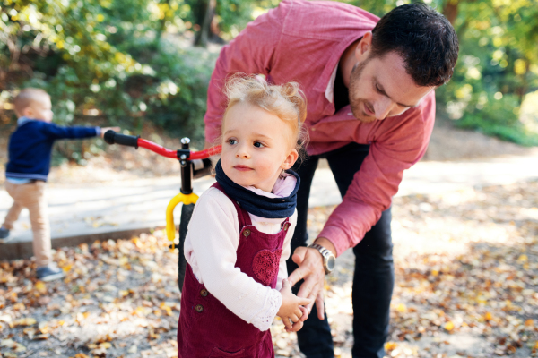 Portraitof father and small twins with balance bikes on a walk in autumn forest.