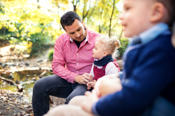 A beautiful young family with small twins on a walk in autumn forest, sitting on log.