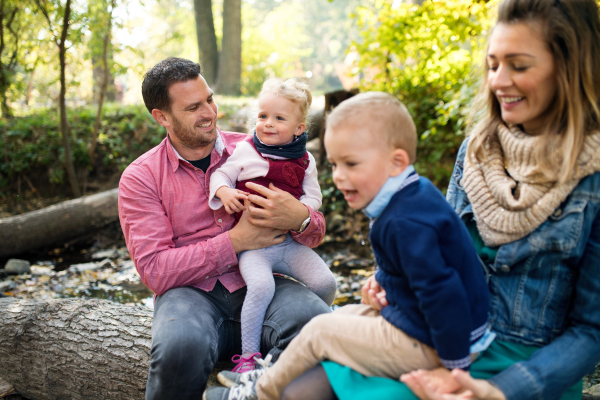 A beautiful young family with small twins on a walk in autumn forest, sitting on log.