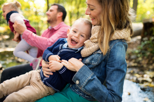 A beautiful young family with small twins on a walk in autumn forest, having fun when sitting.