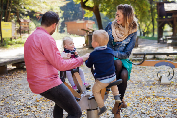 A beautiful young family with small twins playing on playground in autumn.