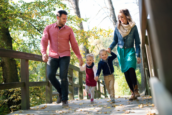 A beautiful young family with small twins on a walk in autumn forest, holding hands.